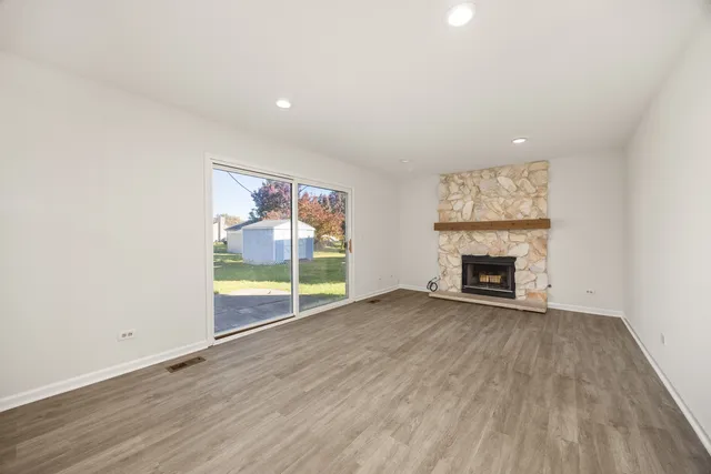 an empty room with wooden floor fireplace and windows