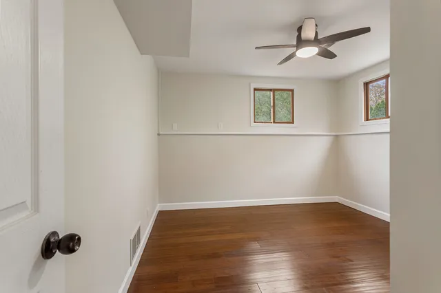 an empty room with wooden floor ceiling fan and windows