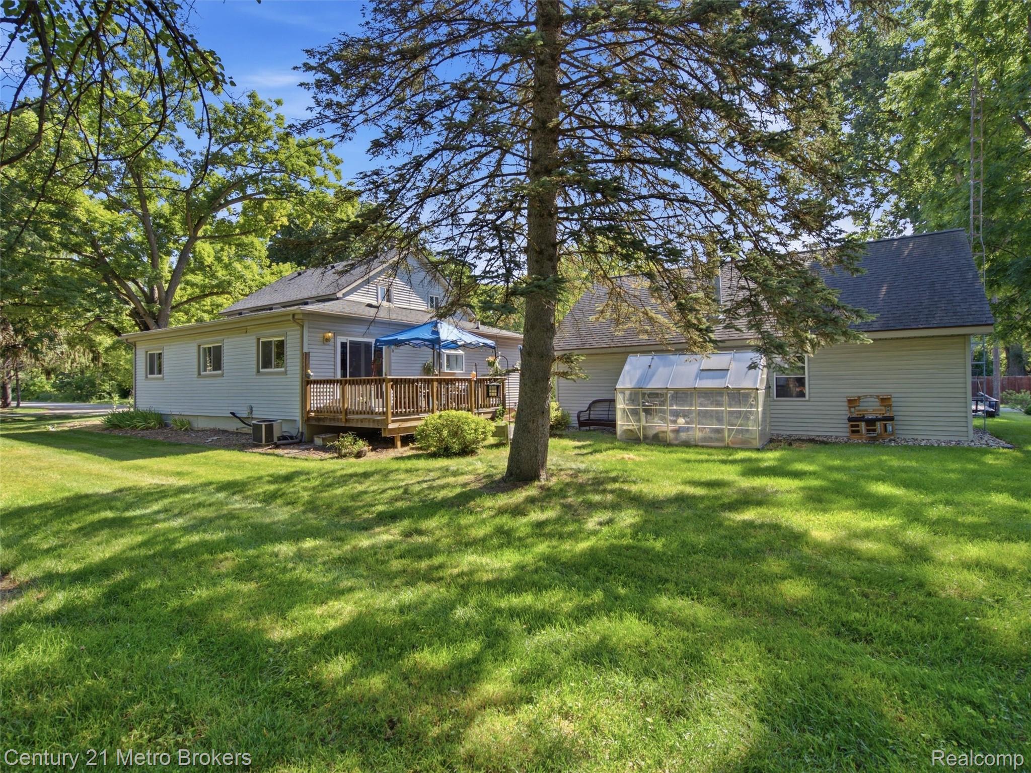 301 Field Road Clio, MI 48420 - Photo 26 of 29 Expansive backyard featuring a wood deck, mature trees, and a clear-paneled greenhouse structure