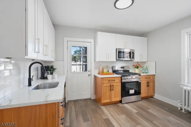 a kitchen with stainless steel appliances granite countertop a stove top oven a sink dishwasher and white cabinets with wooden floor