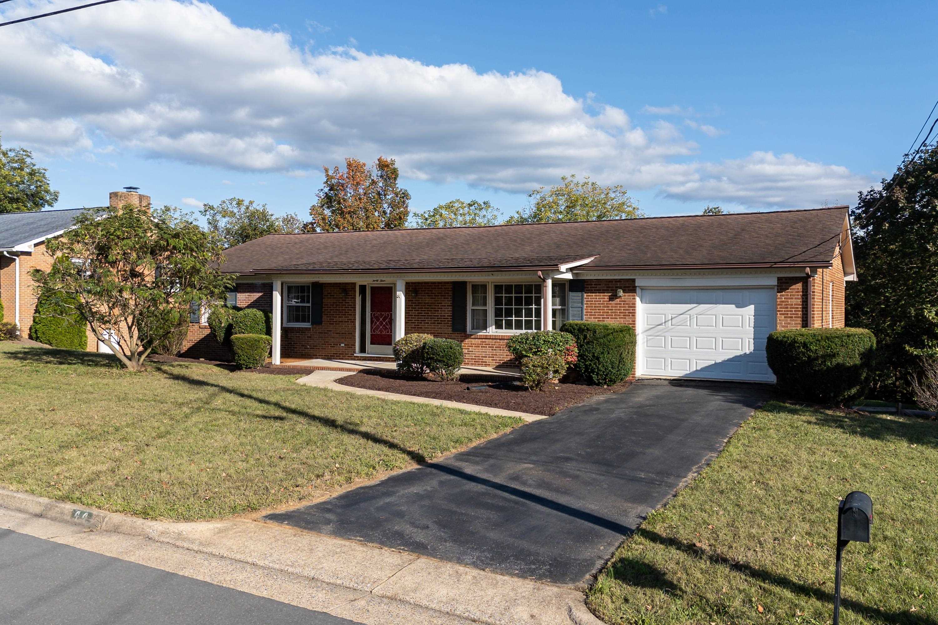 The front view of this lovely home highlights the mature landscaping, paved driveway, single-car garage, and spacious front porch.