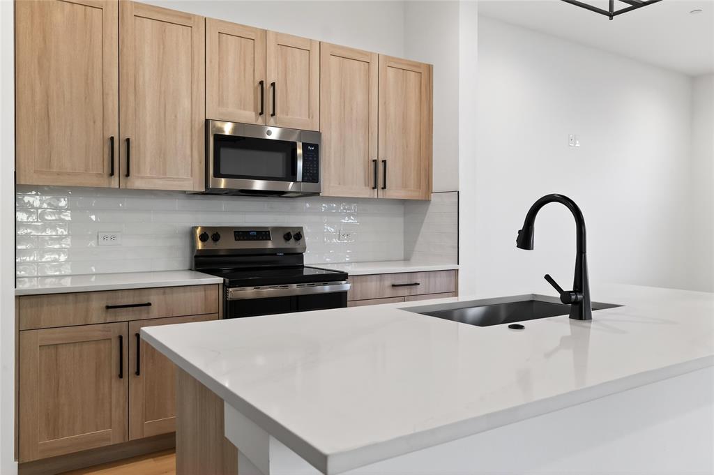 8901 Lowell Street Rowlett, TX 75089 - Photo 7 of 24 Kitchen with stainless steel appliances, light wood finish cabinetry, light stone counters, and tasteful backsplash