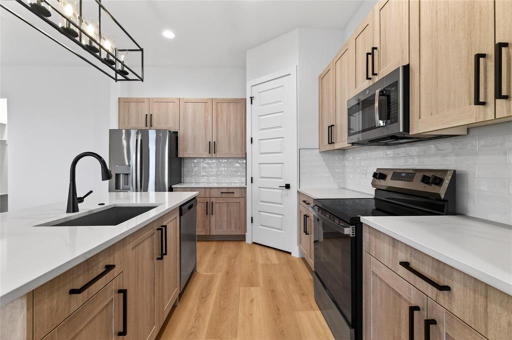8901 Lowell Street Rowlett, TX 75089 - Photo 8 of 24 Kitchen featuring stainless steel appliances, light wood finished floors, light stone countertops, tasteful backsplash, and hanging light fixtures