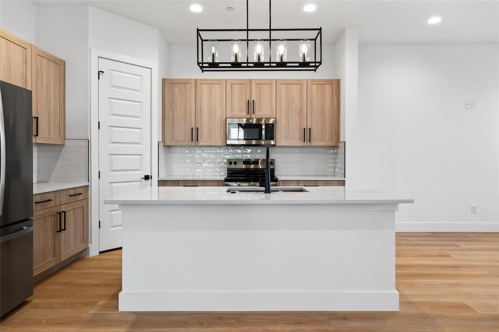 8901 Lowell Street Rowlett, TX 75089 - Photo 10 of 24 Kitchen with light stone countertops, light wood-type flooring, hanging light fixtures, a kitchen island with sink, and stainless steel appliances