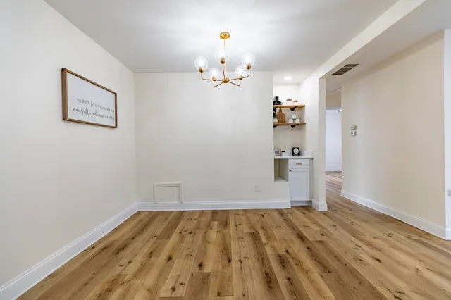 an empty room with wooden floor and way to kitchen