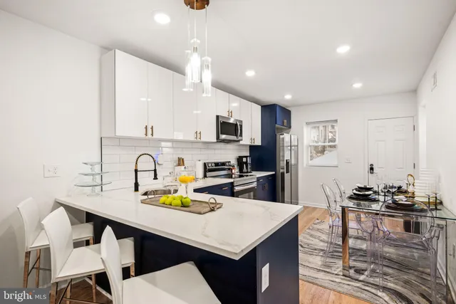 a kitchen with stainless steel appliances kitchen island granite countertop a dining table chairs refrigerator and microwave