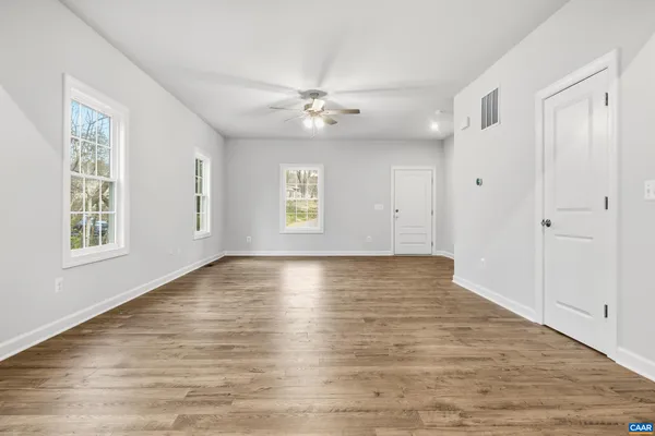 an empty room with wooden floor ceiling fan and windows