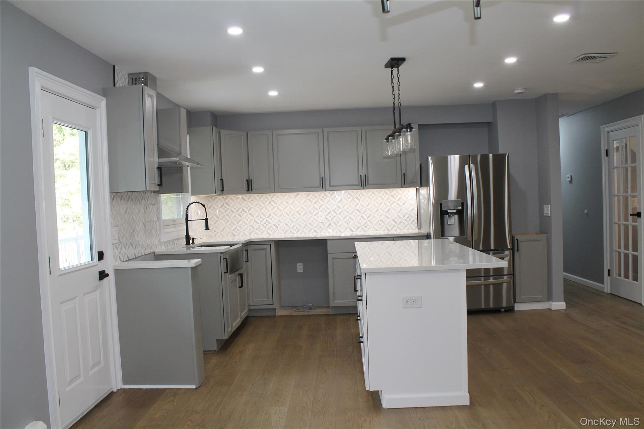 Kitchen featuring decorative backsplash, gray cabinets, stainless steel fridge with ice dispenser, dark wood-style floors, and hanging light fixtures