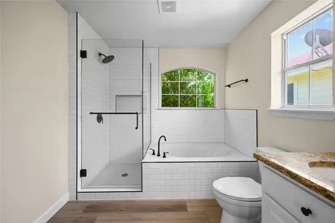 a bathroom with a granite countertop bathtub shower sink vanity and toilet