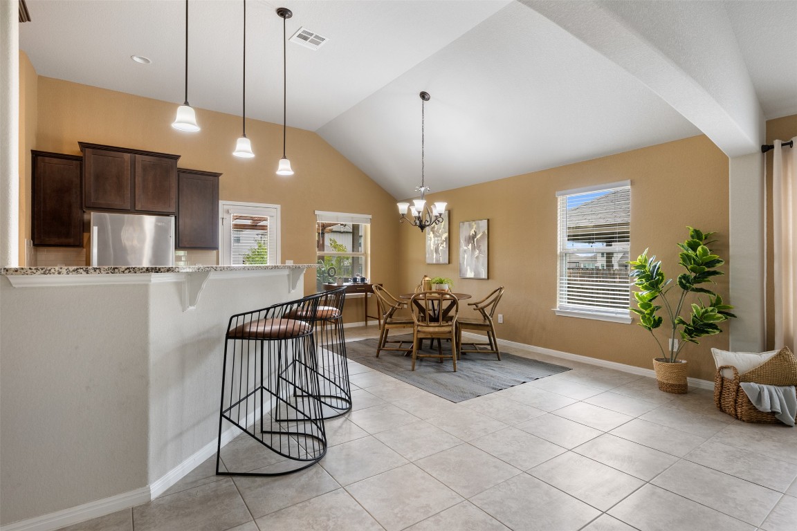 433 Rusk Bluff Avenue Leander, TX 78641 - Photo 5 of 22 Kitchen featuring freestanding refrigerator, light tile patterned flooring, light stone countertops, dark brown cabinets, and a kitchen breakfast bar