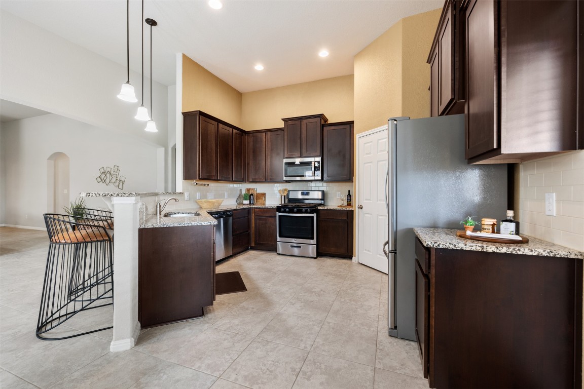 433 Rusk Bluff Avenue Leander, TX 78641 - Photo 6 of 22 Kitchen with stainless steel appliances, dark brown cabinetry, arched walkways, light stone countertops, and light tile patterned floors