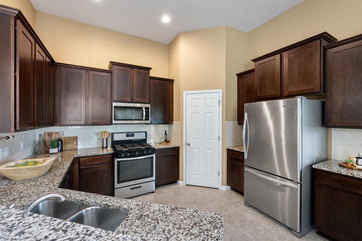 433 Rusk Bluff Avenue Leander, TX 78641 - Photo 7 of 22 Kitchen with stainless steel appliances, dark brown cabinets, tasteful backsplash, light stone countertops, and light tile patterned floors
