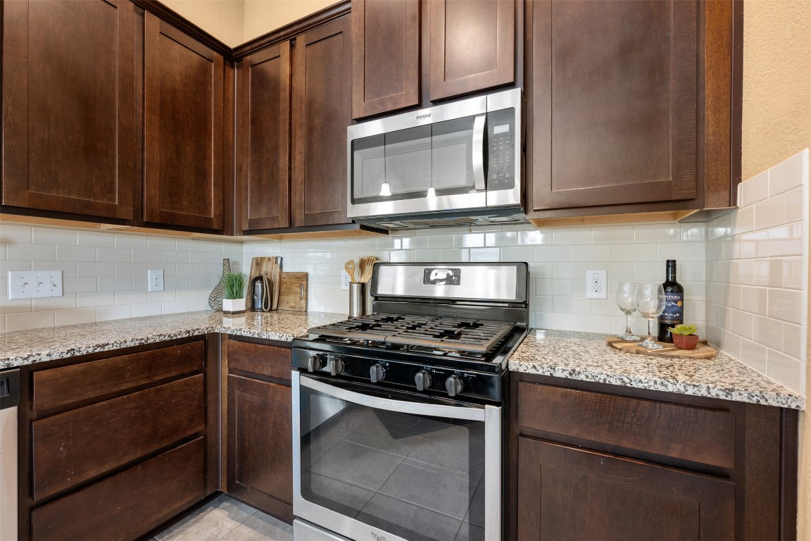 433 Rusk Bluff Avenue Leander, TX 78641 - Photo 8 of 22 Kitchen with appliances with stainless steel finishes, decorative backsplash, dark brown cabinets, and light stone counters