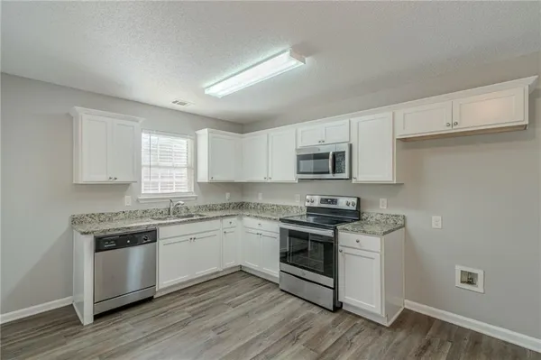 a kitchen with stainless steel appliances granite countertop a stove top oven a sink dishwasher and white cabinets with wooden floor