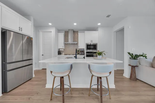 a living room with stainless steel appliances furniture wooden floor and a kitchen view