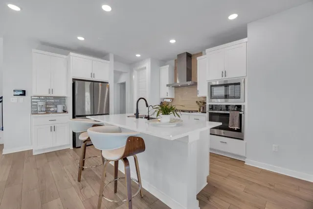 a kitchen with stainless steel appliances granite countertop a refrigerator a sink a stove a dining table and chairs