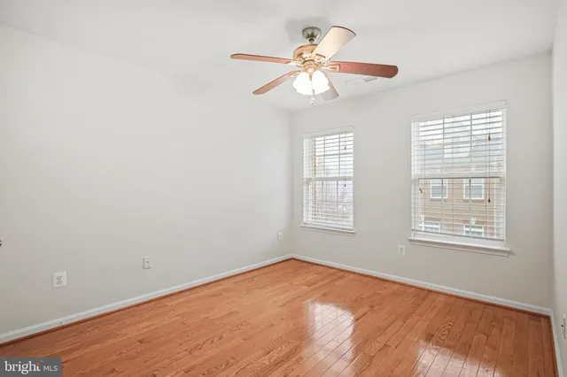 an empty room with wooden floor fan and windows
