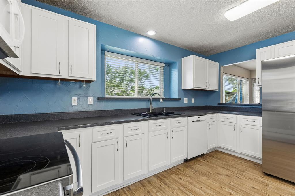 304 Lark Lane Euless, TX 76039 - Photo 11 of 32 Kitchen with dark countertops, stainless steel appliances, white cabinetry, light wood-type flooring, and a textured ceiling