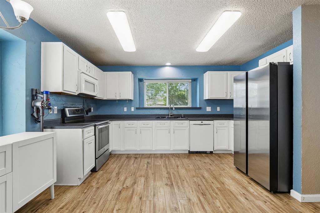304 Lark Lane Euless, TX 76039 - Photo 4 of 32 Kitchen featuring stainless steel appliances, dark countertops, white cabinets, light wood finished floors, and a textured ceiling