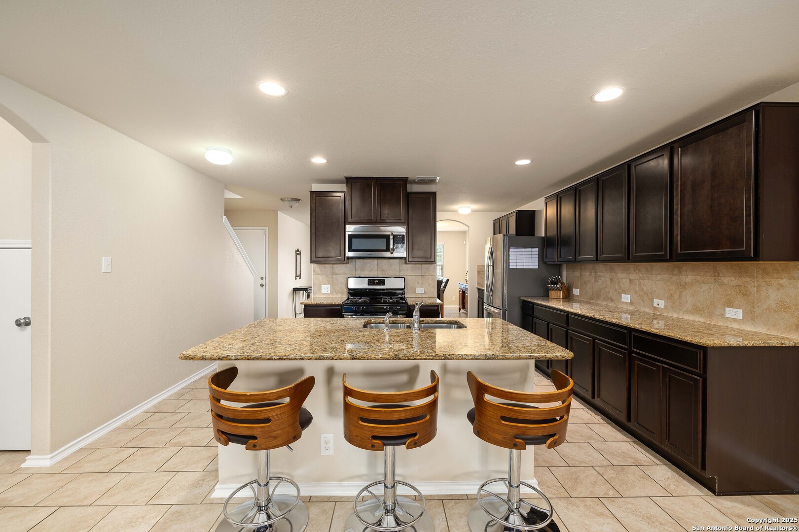 12162 Remilly Way Schertz, TX 78154 - Photo 3 of 18 a kitchen with granite countertop kitchen island stainless steel appliances a stove a sink a microwave a dining table and chairs