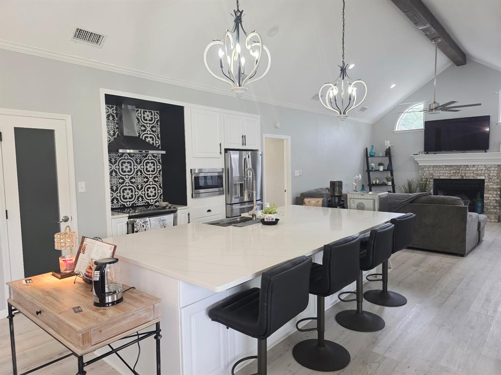 520 Red River Road Belton, TX 76513 - Photo 20 of 36 Open-concept kitchen and living area featuring a large center island with a light-toned countertop, white cabinetry, stainless steel appliances, and a distinct patterned backsplash