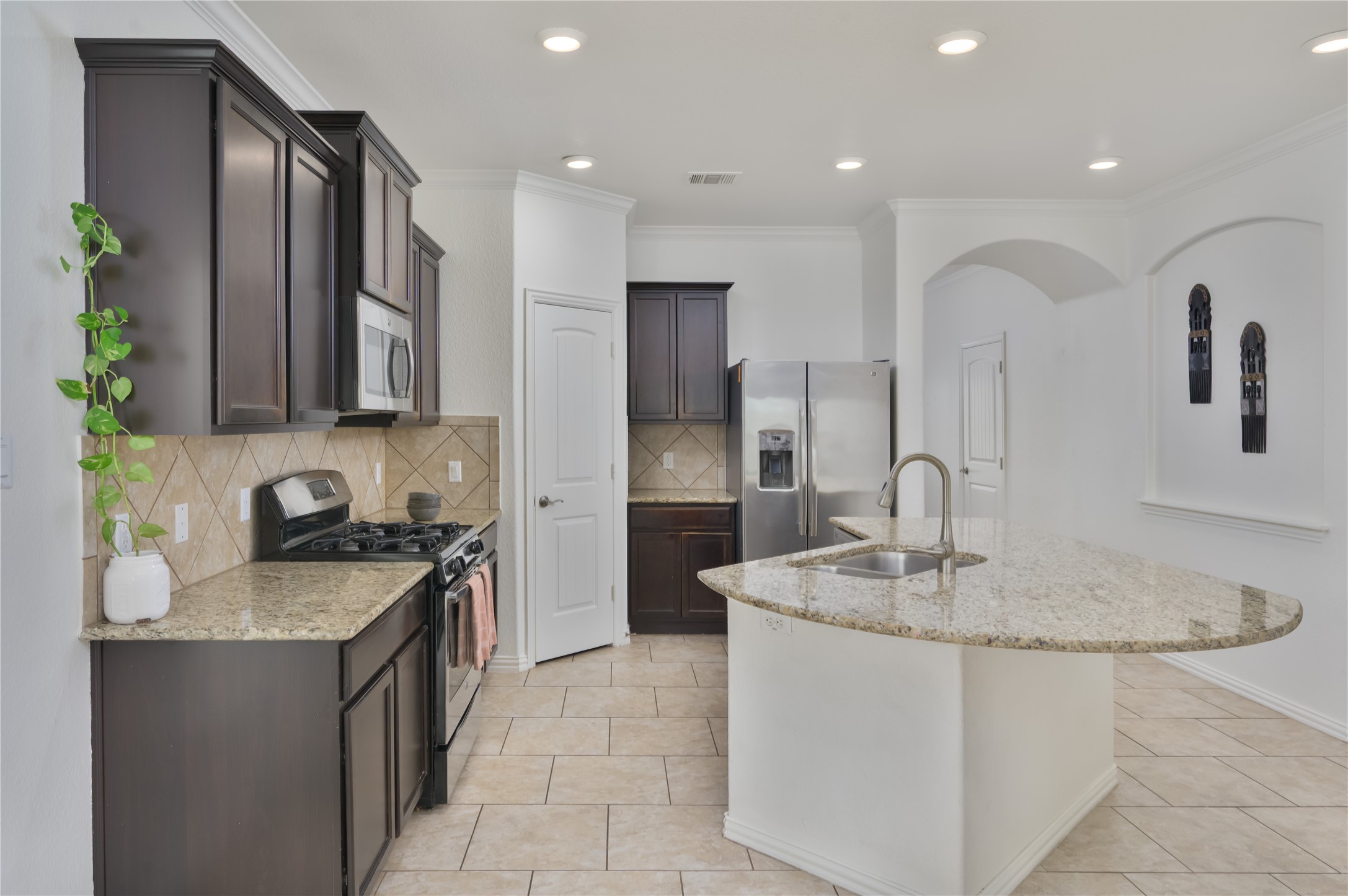 509 Nogales Lane Leander, TX 78641 - Photo 4 of 16 Kitchen with stainless steel appliances, light stone countertops, an island with sink, ornamental molding, and dark wood finish cabinetry