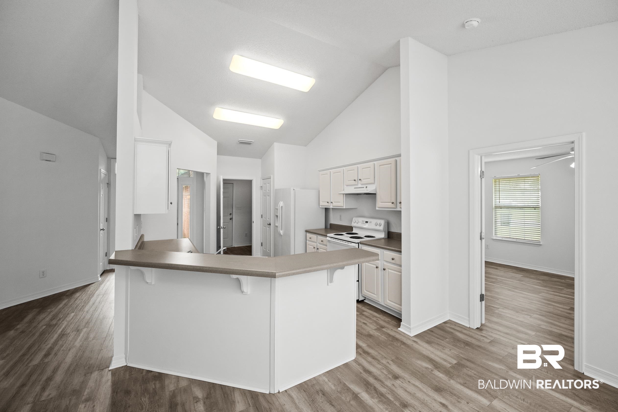 306 Monteith Oaks Drive Foley, AL 36535 - Photo 9 of 38 Kitchen featuring light wood-style flooring, a peninsula, a kitchen bar, white cabinetry, and white appliances