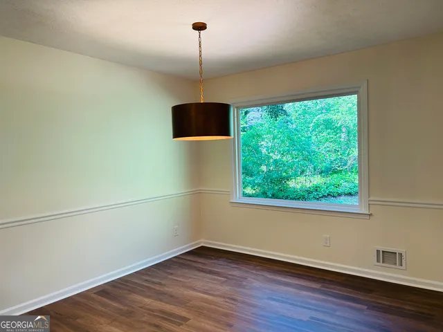 a view of an empty room with wooden floor fridge and a window