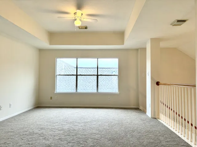 an empty room with chandelier fan and windows