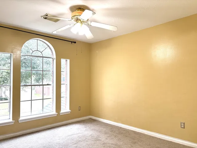 an empty room with windows and chandelier fan