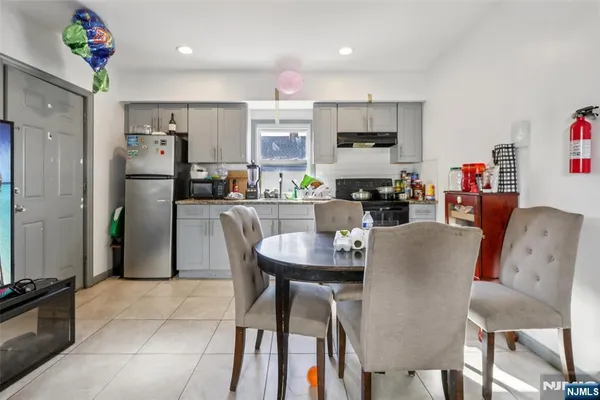 a kitchen with stainless steel appliances granite countertop a dining table chairs refrigerator and sink