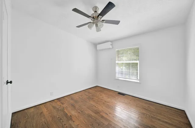 an empty room with wooden floor fan and windows