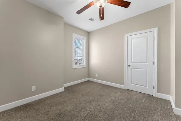 an empty room with chandelier fan and windows