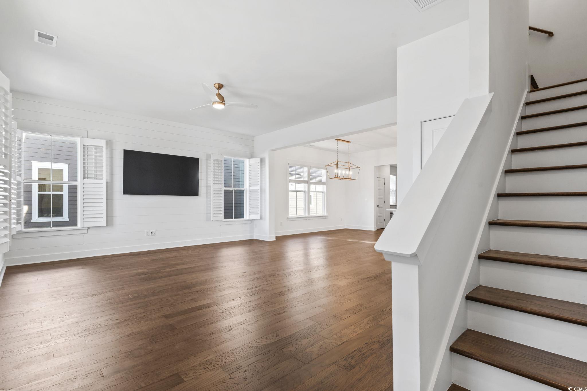 1524 Sayebrook Parkway Myrtle Beach, SC 29588 - Photo 6 of 40 Unfurnished living room with dark wood-style floors, a ceiling fan, stairs, a chandelier, and wooden walls