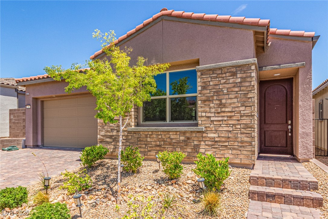 View of front facade featuring stone siding, a tiled roof, an attached garage, stucco siding, and driveway