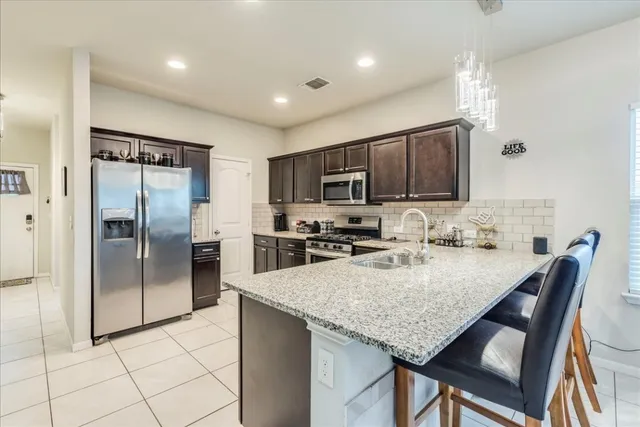 a kitchen with granite countertop a refrigerator a stove a sink a dining table and chairs