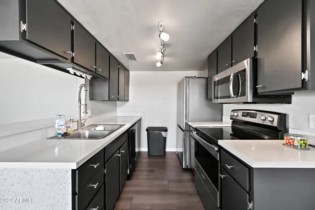 a kitchen with stainless steel appliances a sink dishwasher a stove top oven a refrigerator with wooden cabinets and floor