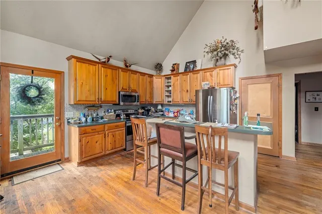 a kitchen with stainless steel appliances granite countertop wooden cabinets a refrigerator a stove a sink and dishwasher with wooden floor