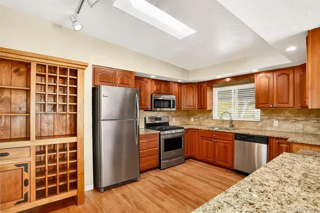 a kitchen with stainless steel appliances granite countertop a refrigerator a sink dishwasher a stove with wooden cabinets and floor