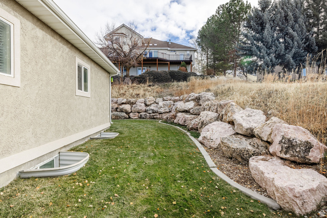 240 Bugle Way Providence, UT 84332 - Photo 7 of 15 Sloped property featuring a rock retaining wall, mature trees, and a stucco exterior with white-framed windows