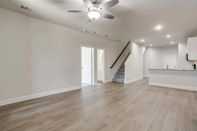 a view of an empty room with wooden floor a ceiling fan and windows