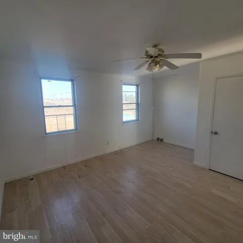an empty room with wooden floor ceiling fan and windows