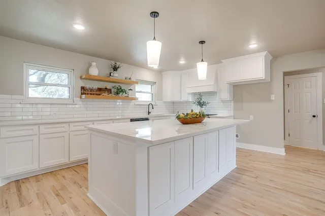 a kitchen with kitchen island white cabinets a sink dishwasher and a stove with wooden floor