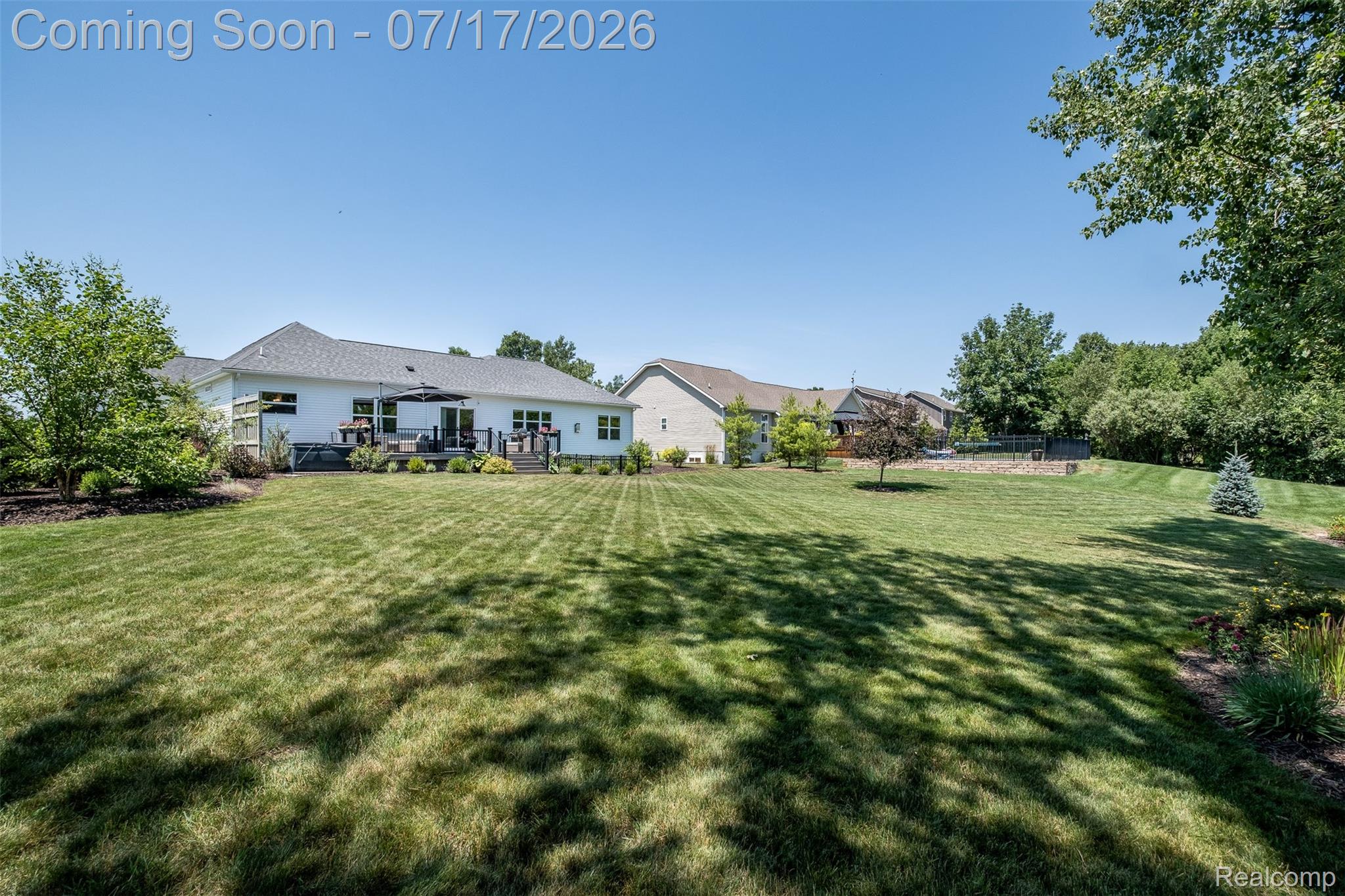 12349 Sugar Maple Drive Fenton, MI 48430 - Photo 57 of 67 Spacious green lawn extending towards a single-story white residence featuring a dark-colored deck and mature trees
