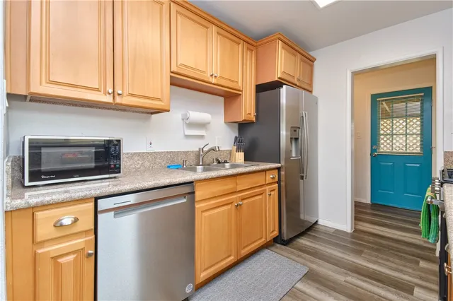 a kitchen with stainless steel appliances granite countertop a refrigerator a sink dishwasher and wooden cabinets with wooden floor