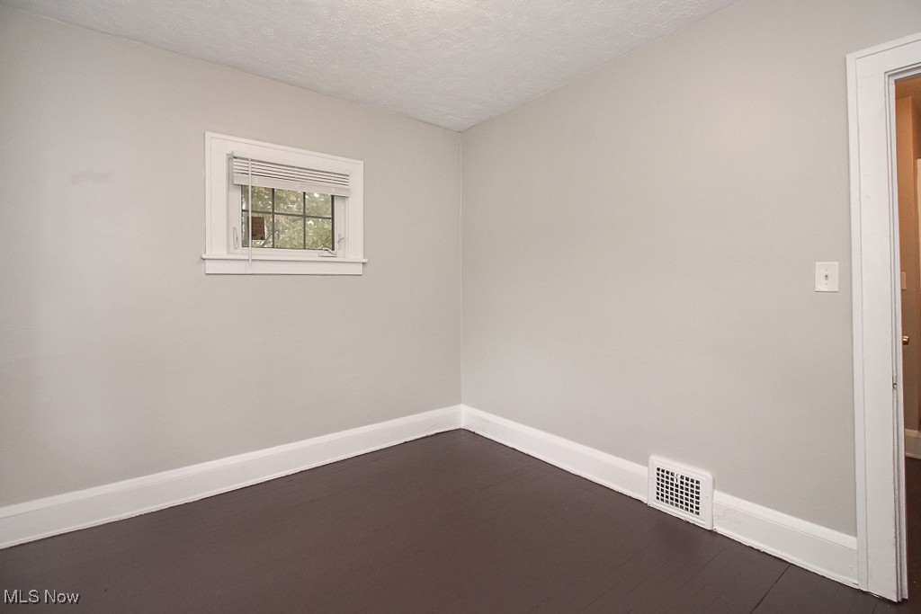 3085 Somerton Road Cleveland, OH 44118 - Photo 13 of 16 Spare room featuring visible vents, baseboards, a textured ceiling, and dark wood-style flooring