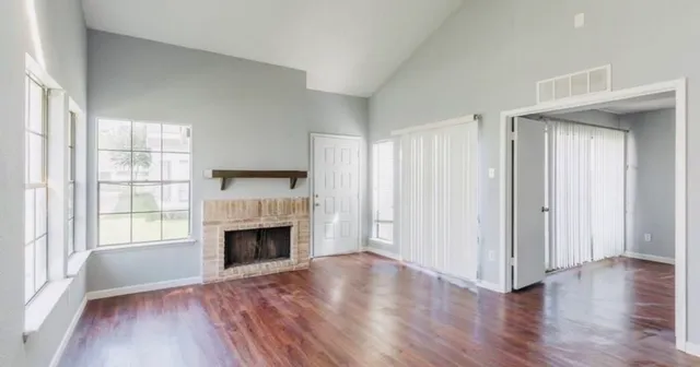 an empty room with wooden floor fireplace and windows