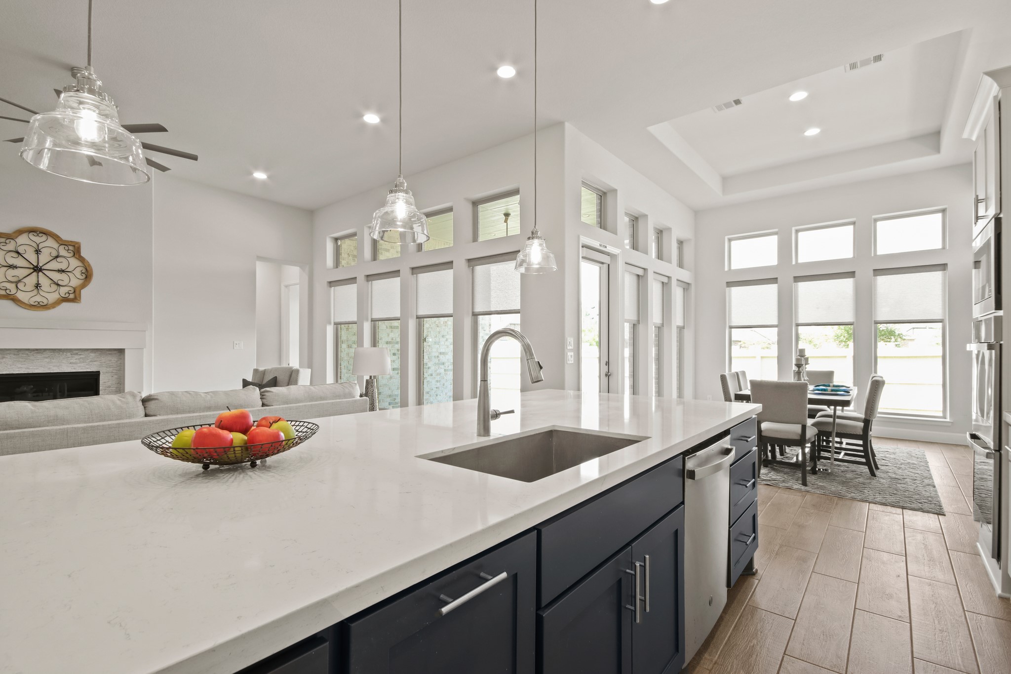 17406 Bayflower Conroe, TX 77385 - Photo 12 of 35 This modern kitchen-living area features a spacious island with a sink, sleek cabinetry, and pendant lighting. It opens to a bright dining area with large windows, offering plenty of natural light. The layout is ideal for entertaining and family gatherings.