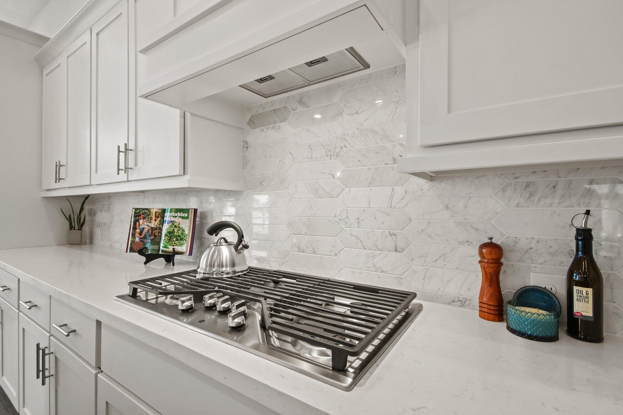 17406 Bayflower Conroe, TX 77385 - Photo 13 of 35 This kitchen features sleek white cabinetry, a modern gas cooktop, and a stylish marble backsplash. The countertop provides ample space, enhanced by contemporary fixtures and subtle decor.