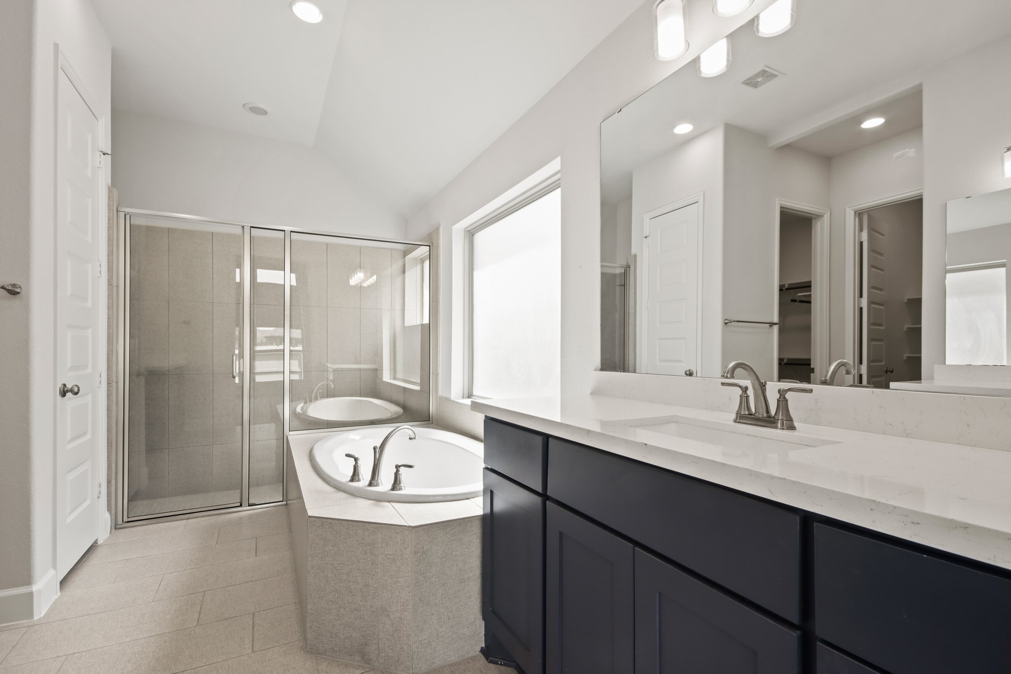 17406 Bayflower Conroe, TX 77385 - Photo 18 of 35 This spacious bathroom features a large glass-enclosed shower, a soaking tub, dual sinks with modern fixtures, and ample natural light from a big window. Perfect for relaxation and functionality.